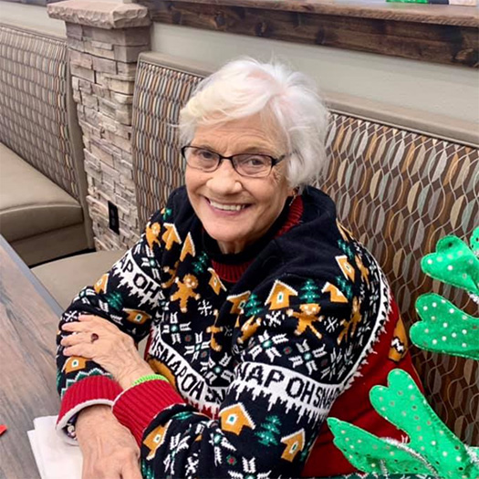 An older woman in a Christmas sweater sitting at a table.