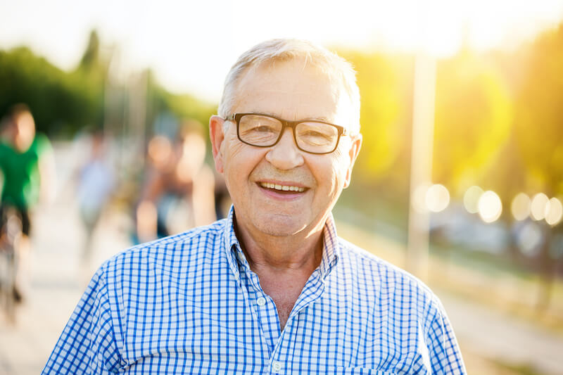An older man smiling in a park.