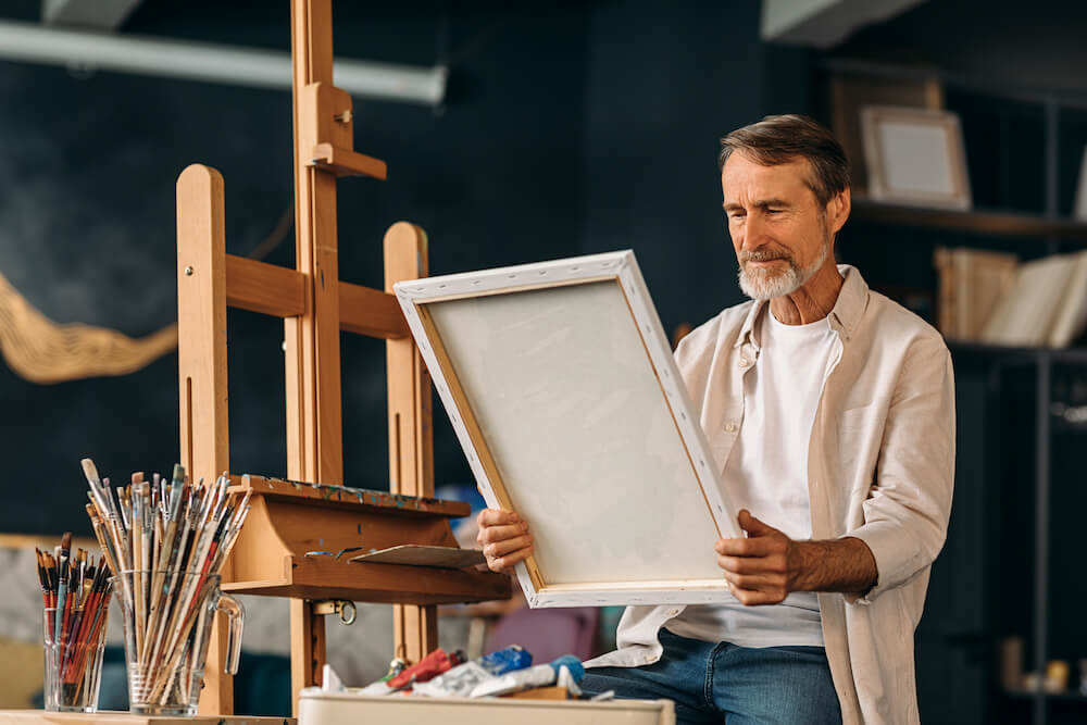 A man sitting in front of an easel looking at a painting.