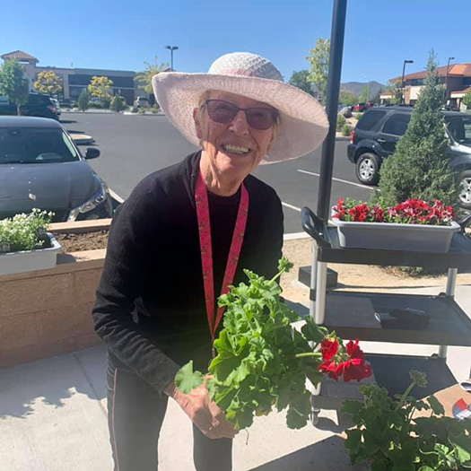An elderly woman in a hat holding a plant in front of a store.