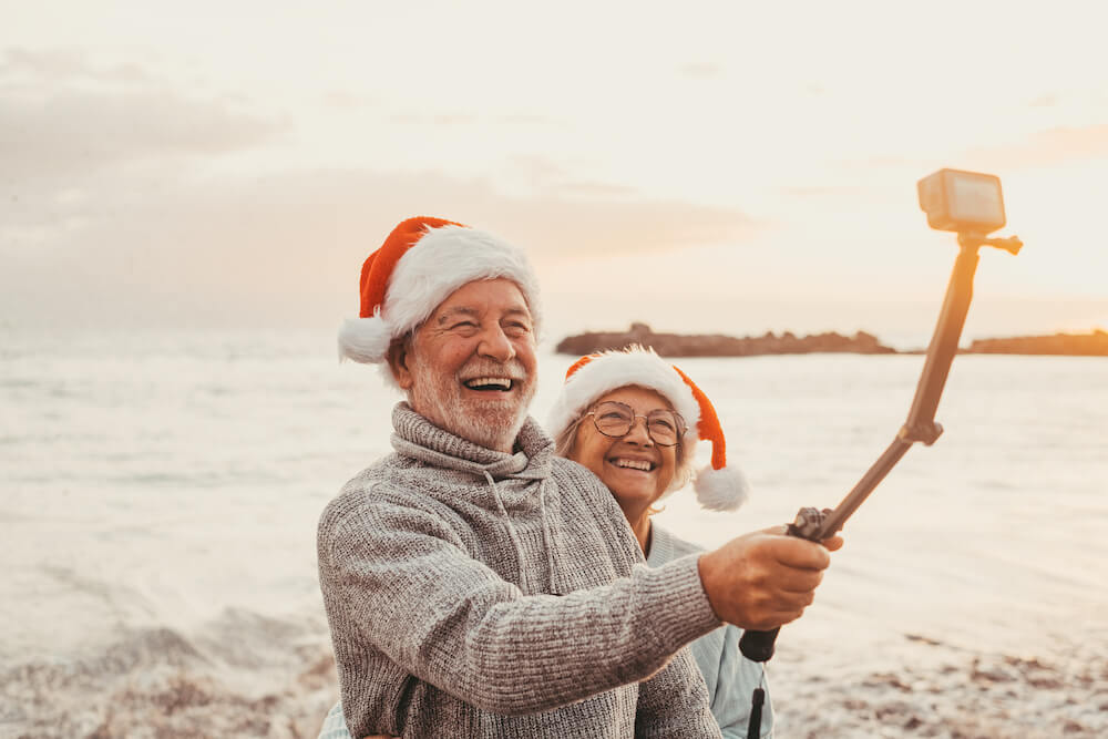 A couple in santa hats taking a selfie on the beach.